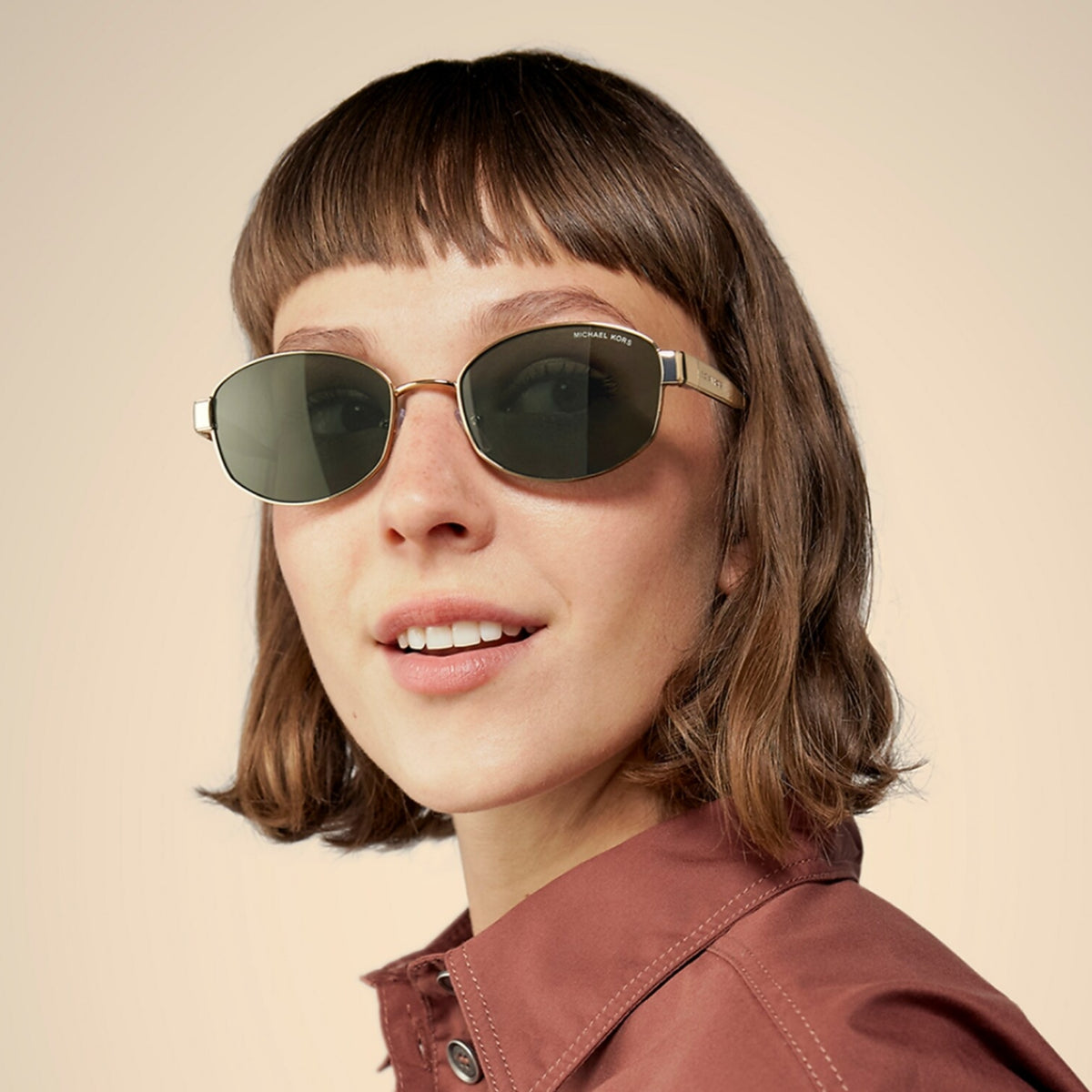 Woman wearing Michael Kors MK1161 light gold oval sunglasses